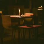Um restaurante com pouca luz e uma mesa destacada com baixa iluminação e duas cadeiras.