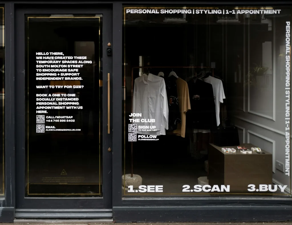 Foto de uma vitrine de uma loja com roupas e adesivos no vidro indicando para os clientes ver, escanear o código e comprar.