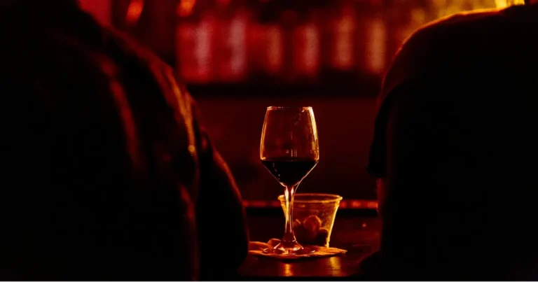 Foto com uma taça de vinho e a silhueta de duas pessoas de costas.