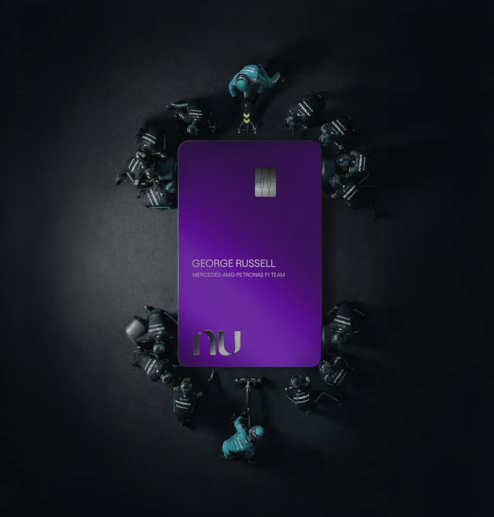 Imagem da equipe da Mercedes-AMG PETRONAS agindo como se estivessem trocando os pneus de uma Formula 1, porém há um cartão da Nubank ao invés do carro