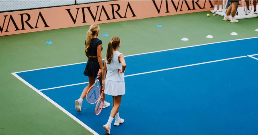 Duas mulheres em uma quadra de tênis com destaque para a logo da Vivara na lateral da quadra