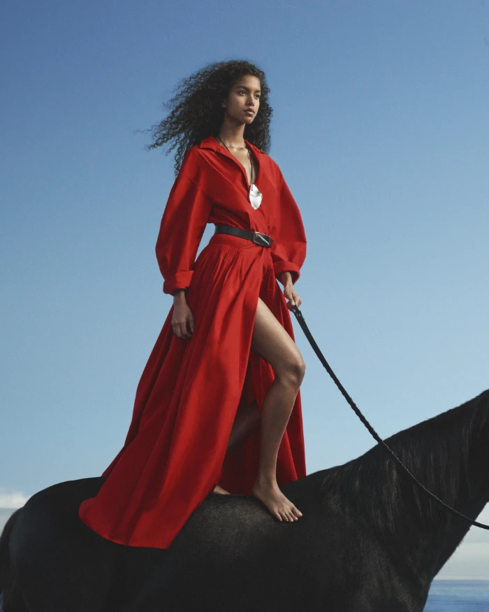 Uma mulher negra com um vestido longo vermelho em cima de um cavalo preto