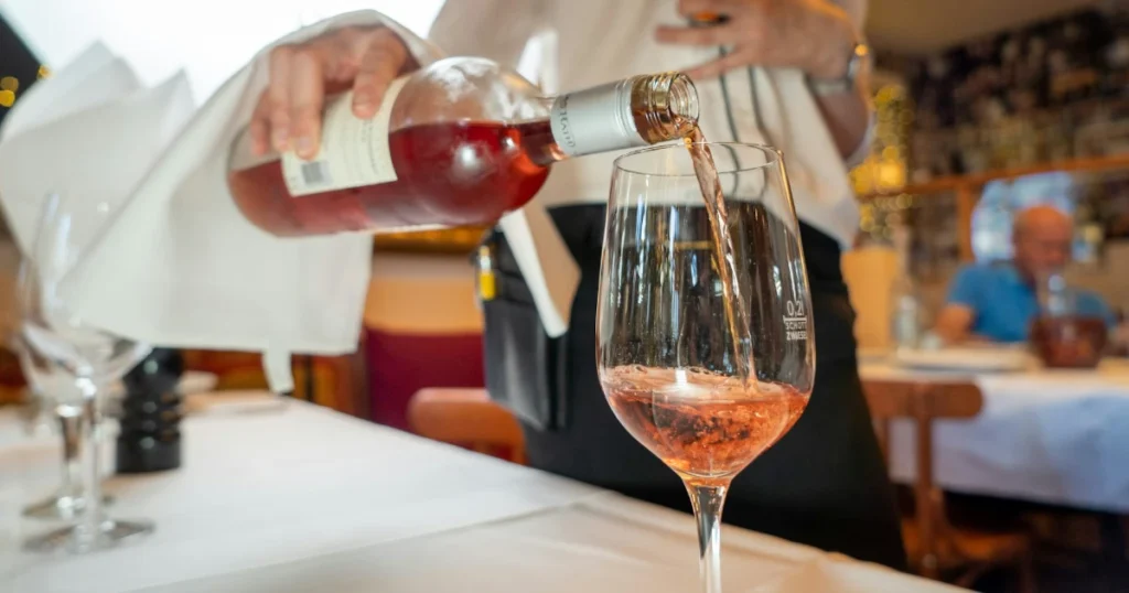 Foto de uma pessoa servindo uma taça de vinho rosé em um restaurante