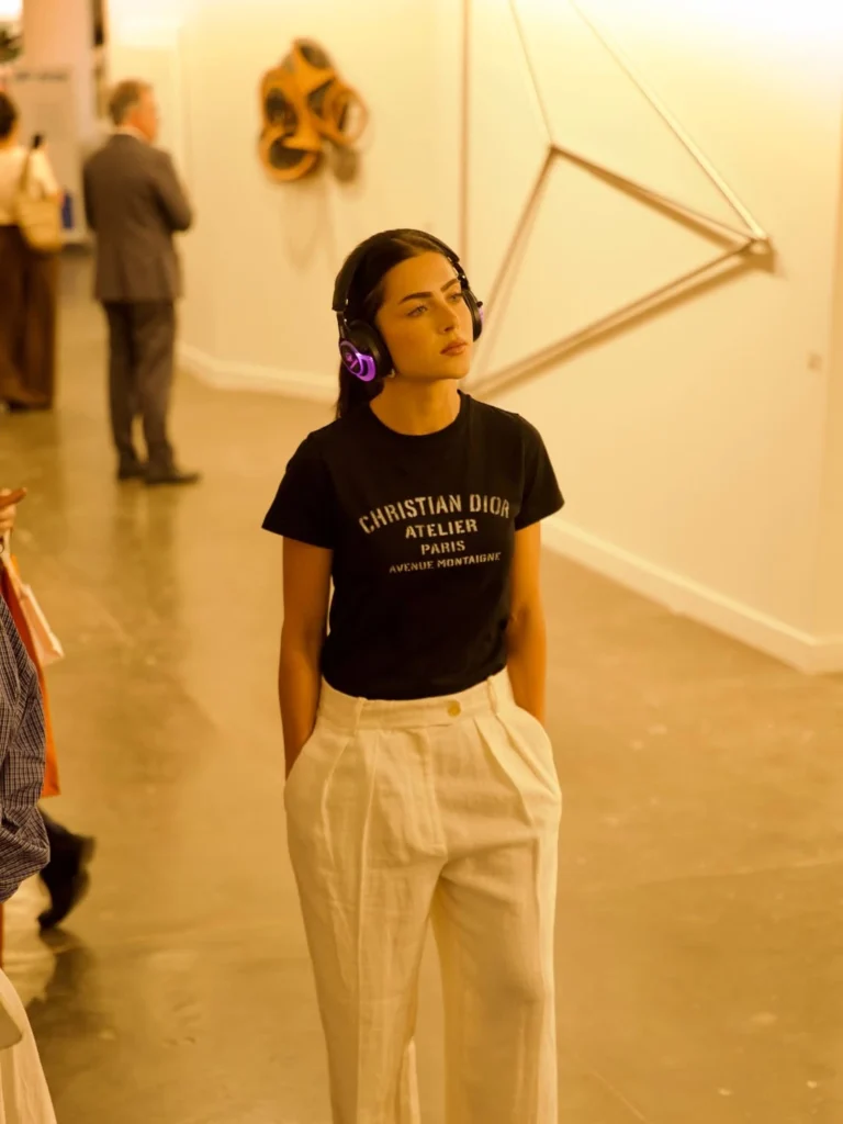 Foto da Jade Picon, uma mulher branca, cabelos pretos, com fone de ouvido grande, camiseta preta e calça branca.