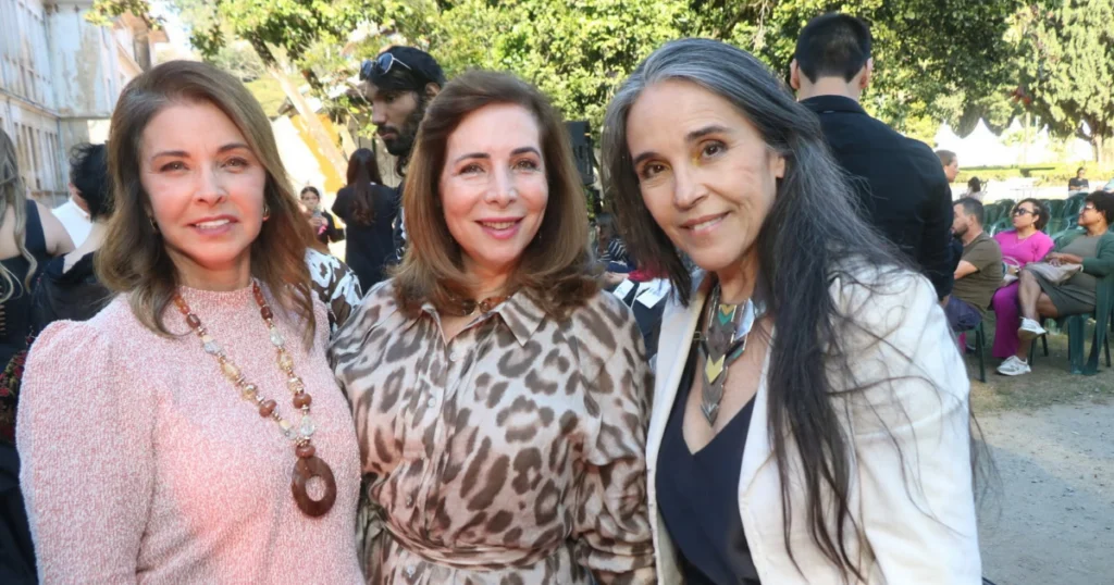 Jussara Medrado é curadora do Vale Fashion, uma mulher branca, com cabelos pretos, blazer branco e blusa preta por baixo