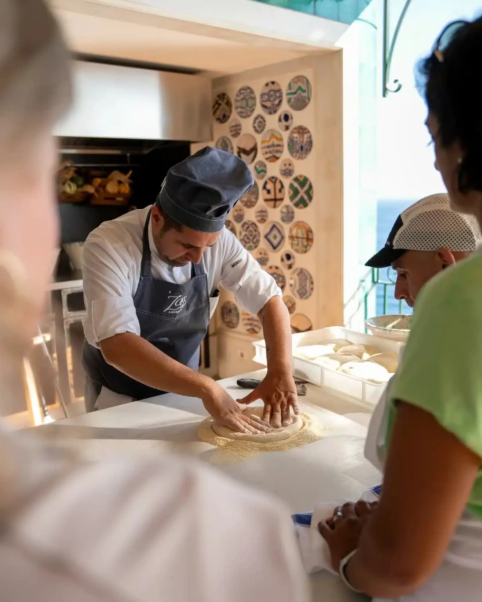 Foto de um pizzaiolo amassando uma massa de pizza enquanto hóspedes do Hotel Il San Pietro Positano observam