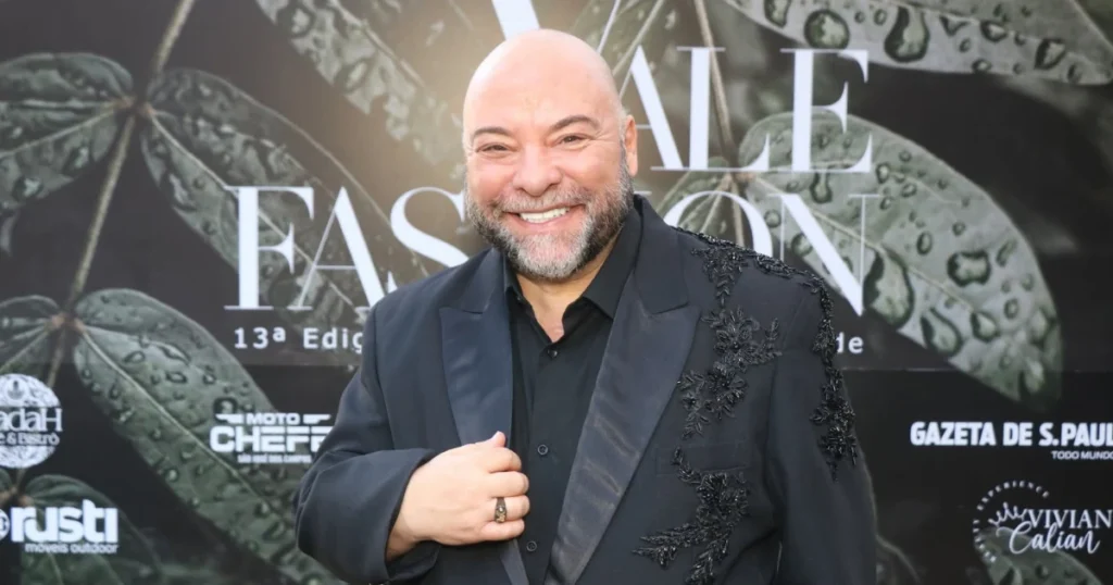 Foto do Willian Roggles, um homem branco, vestido de terno preto, na frete do backdrop do Vale Fashion
