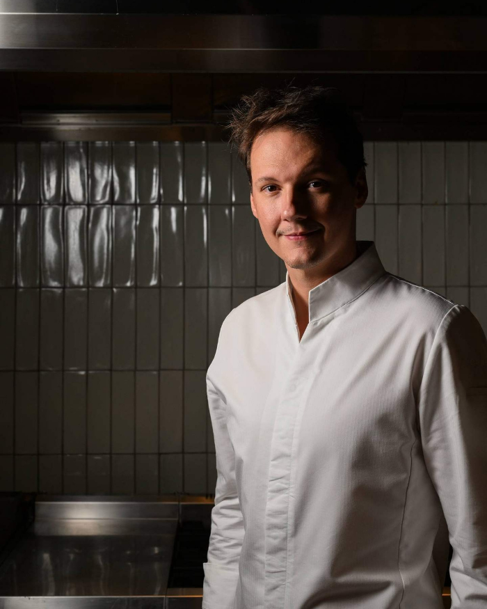 Foto do Chef Ian Baiocchi do Grupo Íz, um homem branco, cabelos pretos, vestido como um chef de cozinha