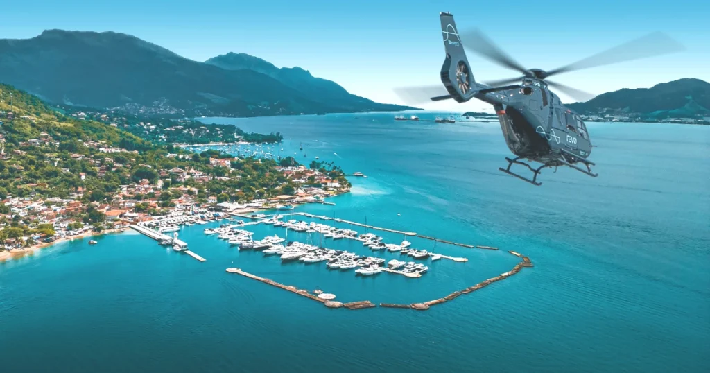 Imagem de um helicóptero da Revo sobrevoando uma costa com diversos barcos ancorados