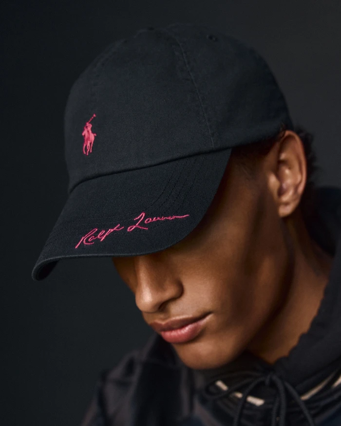 Foto do rosto de um homem negro com um boné preto com a logo rosa da Ralph Lauren